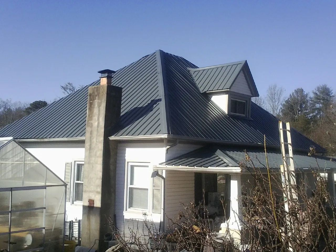 Dark blue standing seam metal roof on a white farmhouse with dormer — Slate & Tile Roof Repair by Roofing Brothers in Mount Carroll