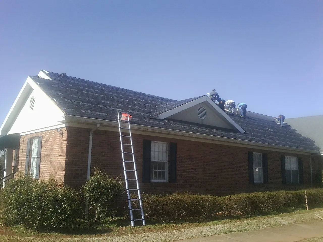 Crew tearing shingles off a brick ranch roof with a ladder set — Metal Roof Repair work by our crew in Mount Carroll