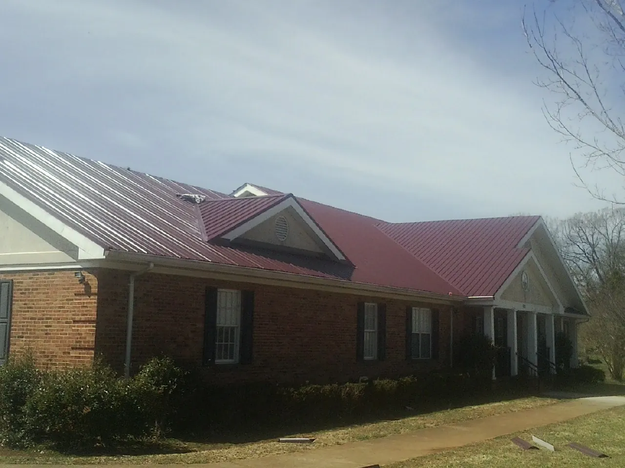Red metal roof with gabled entries on a long brick building, from a Hail Damage Roof Repair job in Mount Carroll