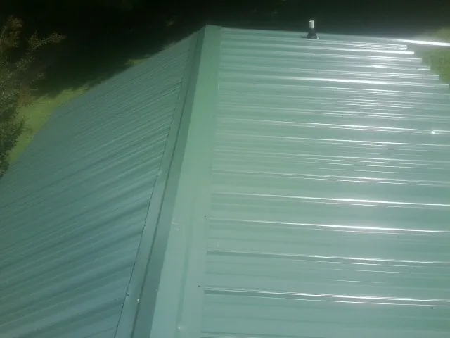 New green metal panels meeting at the ridge of a roof — Flat Roof Repair work by our crew in Mount Carroll