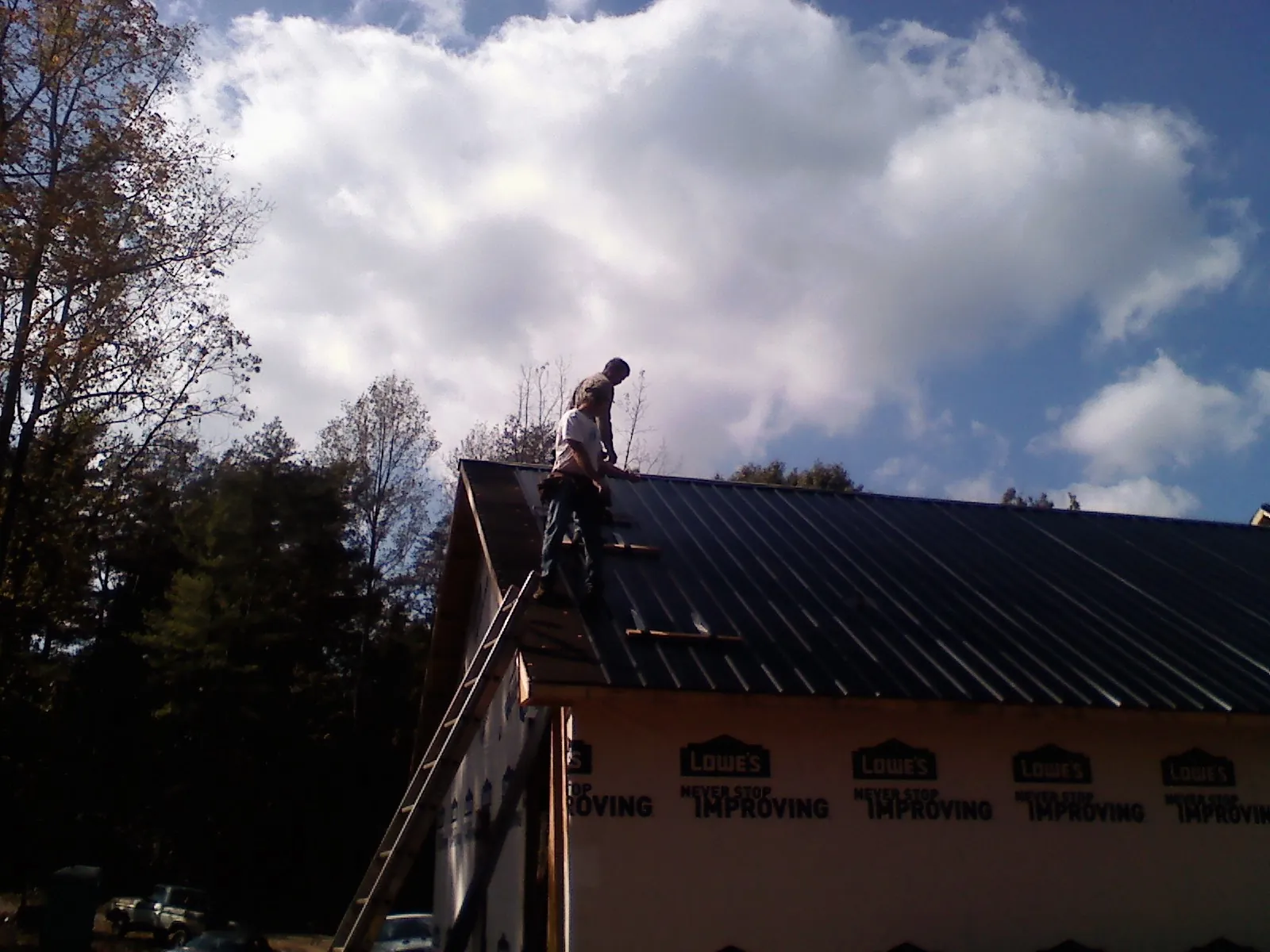 Roofer fastening dark metal panels high against a cloudy sky, from a Roof Inspection job in Mount Carroll