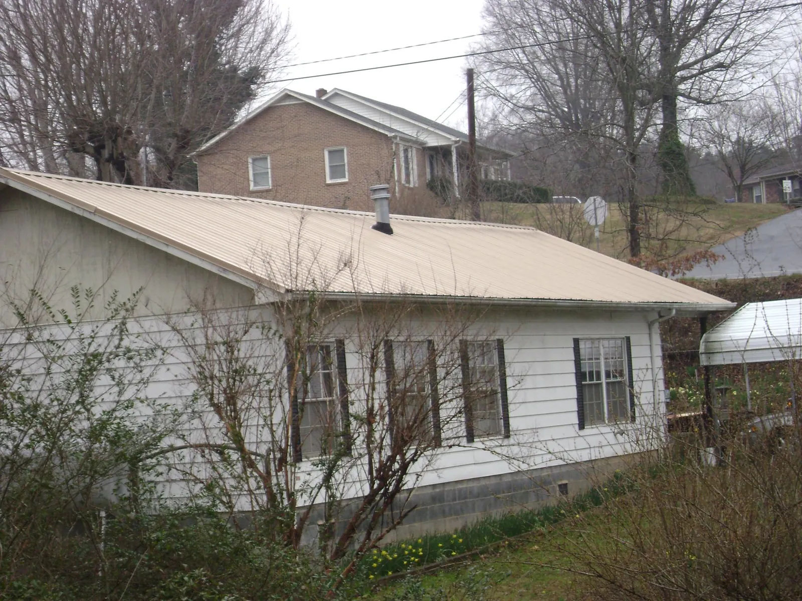 Tan metal roof on a white sided house set into a hillside — Commercial Roofing by Roofing Brothers in Mount Carroll